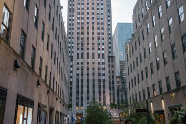 New York City, New York, ABD - 07.29.2024: Rockefeller Centers kulesinin manzarası meydanda dükkanları ve bahçeleri olan binalar tarafından çerçevelenmiştir. Akşam ışığı ve şehir mimarisi Manhattan 'ın merkezinde huzurlu bir şehir atmosferi yaratıyor..