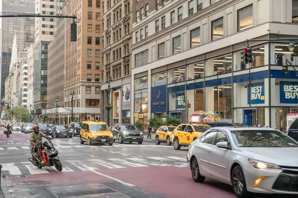 New York, New York, New York, ABD - 07.29.2024: Arabaları, taksileri ve büyük bir Best Buy mağazasının önünde scooter 'ı olan hareketli bir New York caddesi. Şehir manzarası bulutlu bir gökyüzü altında hareketli ve modern mağazalarla dolu..
