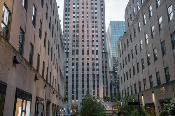 New York City, New York, ABD - 07.29.2024: Rockefeller Centers kulesinin manzarası meydanda dükkanları ve bahçeleri olan binalar tarafından çerçevelenmiştir. Akşam ışığı ve şehir mimarisi Manhattan 'ın merkezinde huzurlu bir şehir atmosferi yaratıyor..