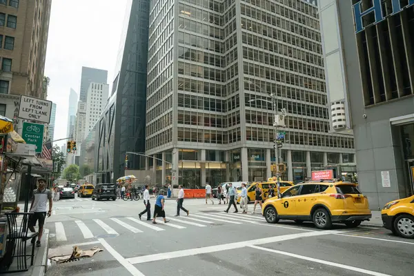 New York, New York, New York, ABD - 07.29.2024: New York Midtown 'da işlek bir cadde kavşağı insanların sarı taksiler ve uzun cam binalar arasından geçtiğini gösteriyor. Şehir hayatı hareketli, mimari ve ticaretle dolu..