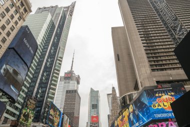 New York City, New York, ABD - 07.29.2024: Times Meydanı 'nda bulutlu bir gökyüzüne karşı yüksek binalar yükseliyor. Reklam panoları ve cam cepheleri şehirlerin enerjisini yansıtıyor.