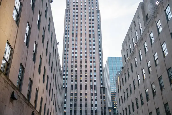 Rockefeller Center kulesinin merkezli görüntüsü, simetrik taş ofis binaları tarafından sıkıca çerçevelenmiş. Görüntü, Manhattan şehir merkezinin Art Deco tasarımı ve şehir yoğunluğunu vurguluyor.