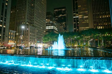 Manhattan 'da, göz kamaştırıcı bir çeşme geceleri gökdelenlerle çevrili mavi ışıkla parlar. İnsanlar suyun üzerinde yürüyor, şehrin canlı atmosferinin tadını çıkarıyorlar..