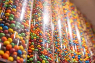 Farklı renklerde şekerlemelerle dolu saydam borular. Mağazanın içinde parlak ve neşeli bir şeker duvarı.