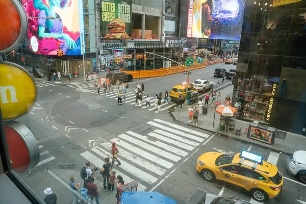 New York City, New York, ABD - 07.29.2024: Turistler ve yerel halk Times Meydanı 'nda renkli dijital reklam panolarının altında kalabalık bir caddeyi geçiyor. Sarı taksiler insanlar yükselen reklamların altında yürürken bekliyor..