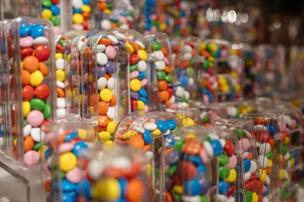 Parlak renkli şekerler şeffaf harf şekilli konteynırlara doldurulur. Yakın çekim bir perakende veya hediyelik eşya dükkanında canlı bir şeker sergisi gösteriyor.