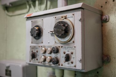 Etiketli göstergeleri ve düğmeleri olan eski bir jiroskop kontrol panelinin yakın çekimi. Cihaz, bir askeri veya deniz gemisinin içindeki bir duvara monte edilmiş..