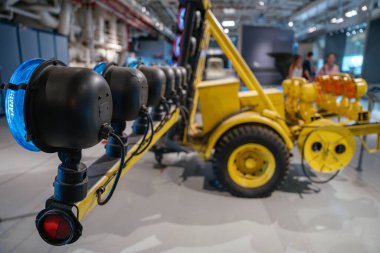 Yakın plan çekimde sarı bir havaalanına veya taşıyıcı römorka monte edilmiş mavi ve kırmızı ışıklar görülüyor. Arka plan, karavanın geri kalanını ve müze ortamını gösteriyor..