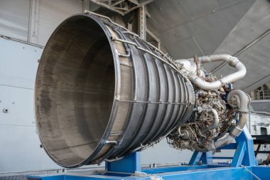 Görünür nozül, borular ve turbo pompa bileşenleriyle güçlü bir roket motorunun yakın çekim görüntüsü. Motor, teşhir amacıyla mavi bir metal çerçeveye monte edilmiştir..