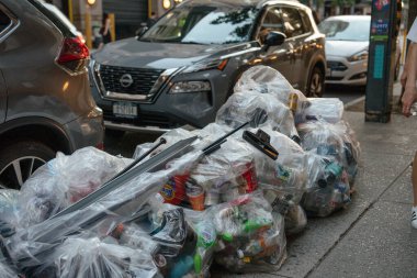 New York City, New York, ABD - 07.30. 2024: Geri dönüşümlü kutular, şişeler ve ambalajlarla dolu sıkıca paketlenmiş temiz plastik torbalar şehir kaldırımına istiflenmiştir. Fotoğraf kentsel atık ayrımı ve sokak seviyesindeki geri dönüşümü ayrıntılı olarak yakalıyor.