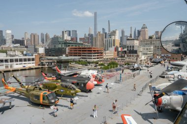 New York City, New York, ABD - 07.30. 2024: Intrepid Müzesi 'nin güvertesinde bir askeri helikopter ve jet koleksiyonu sergilenmektedir. Manhattan silueti çarpıcı bir kentsel zemin oluştururken, turistler sergiyi keşfediyorlar.