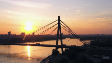 Araba trafiği olan bir nehir köprüsünün yan görüntüsü. Akşam gün batımı gökyüzü.