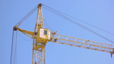 Mavi arka planda sarı bir kule vincinin arka görüntüsü. Sola dön..