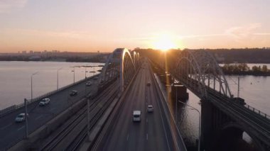 Köprü üzerinde hareket eden arabalarla güzel bir şehir manzarası. Demiryolları ve karayolları ile nehir köprüsünün üst manzarası.