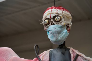 Kanlı bandajlı ve mavi cerrahi maskeli perili bir iskeletin detaylı portresi. Tıbbi temalı cadılar bayramı bahçesi dekorasyonu çatının altında çekildi..