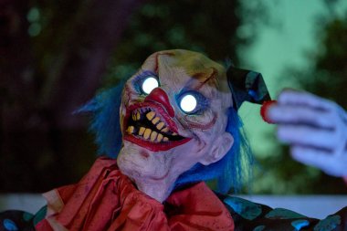 Mavi saçlı, parlak sarmal gözlü şeytani bir palyaçonun yakın plan portresi. Kırmızı burun, sarı dişler ve sert ışıklandırma korkunç bir Cadılar Bayramı gösterisi yaratır..