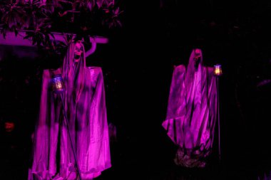 Kapüşonlu Azrail figürleri geceleri parlayan fenerler tutar. Mor ışıklandırma ve örtülü kumaş ürkütücü bir cadılar bayramı manzarası yaratır..