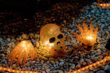 Aydınlanmış kafatası ve iskelet eller turuncu halat lambalı çakıl taşlarının üzerinde dinleniyor. Ürkütücü cadılar bayramı bahçesi dekorasyonu ve geceleri tüyler ürpertici parlaklığı.