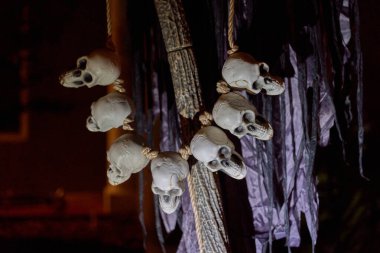 Küçük kafatasları bir ipe asılır ve geceleri yırtık kumaşa asılır. Huysuz ışıklandırmalı bir Cadılar Bayramı dekorunun ürkütücü yakın plan detayları.