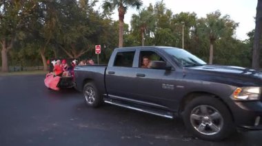 Orlando, Florida, ABD - 10.30.2024: Bir kamyonet okul otoparkından kostümlü ailelerin karavanını çekiyor. Toplum alacakaranlıkta şenlikli bir gezintinin keyfini çıkarıyor..