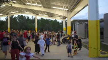Orlando, Florida, ABD - 10.30.2024: Kostümlü büyük bir ebeveyn ve çocuk kalabalığı kapalı bir okul köşkünün altında toplanıyor. Açık hava halk kutlamasında şaka mı şeker mi çantaları, bebek arabaları ve dostça sohbetler yer alıyor..