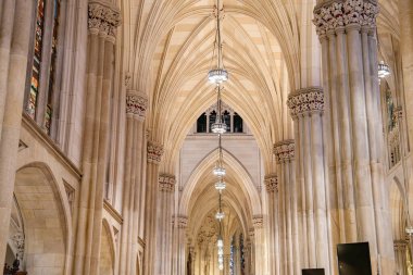 Gotik tarzı bir katedralin içindeki zarif taş sütunların ve tırtıklı kemerlerin yakın görüntüsü. Mimari, yumuşak ışıklandırma ve detaylı vitray pencerelerle geliştirilmiştir..