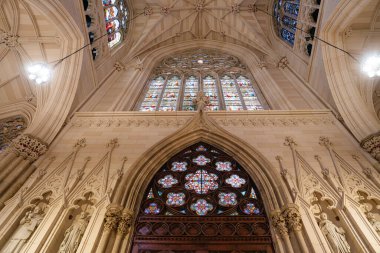 Görüntü, New York 'taki St. Patrick Katedrali' ndeki vitray pencereler, sivri kemerler ve taş heykellerin detaylı bir görüntüsünü yakalıyor. Gotik mimaride karmaşık oymalar, dini heykeller ve canlı dekoratif elementler yer alıyor.