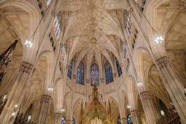 Bu görüntü, New York 'taki St. Patricks Katedrali' nin üzerinde yükselen kubbeli tavanı ve karmaşık vitray pencereleri yakalar. Çarpıcı Gotik mimari, tırtıklı kemerler, dekoratif taş işçiliği ve çevre aydınlatmasıyla zenginleştirilmiştir..