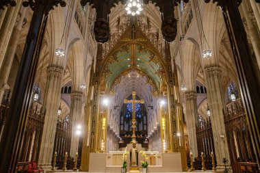 Bu resim, New York 'taki St. Patricks Katedrali' nin merkezindeki altın haçı ve ana sunağı gösteriyor. Yükselen kolonlar, tırtıklı kemerler, boyalı camlar ve zarif aydınlatmalarla çevrili Gotik Diriliş 'in hem görkemli hem de kutsaldır..