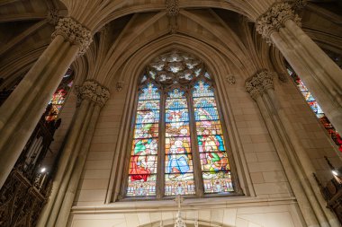 Gotik tarzda bir katedralde göz kamaştırıcı bir vitraydı. İncilsel sahnelerin canlı renkleri vardı. Uzun taş sütunlar ve detaylı kemerler kutsal sanat eserini çerçeveleyerek görkemli ve saygılı bir ortam yaratıyor..