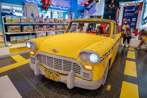 New York, New York, New York, ABD - 07.31.2024: Bu tam görüş, içinde insanların oturduğu gerçek boyutta bir LEGO taksi modelini gösteriyor. Ayrıntılı heykel, set ve oyuncu dekorlarla çevrili bir LEGO mağazasında gösteriliyor.