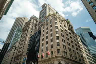 Beşinci Cadde 'ye bakan çarpıcı bir manzara, tarihi binaların yanında Amerikan bayrakları ve parlak cam gökdelenler gösteriyor. Parlak mavi gökyüzü altındaki eski ve yeni mimarinin kontrastı Midtown Manhattan karakterini yansıtır..