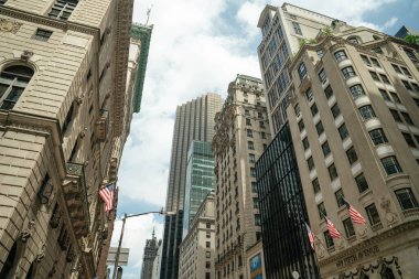 Yukarı bakan bir manzara, Manhattan 'ın ortasındaki Beşinci Cadde boyunca uzanan tarihi taş binalarda Amerikan bayraklarını yakalıyor. Mimari tarzların karşıtlığı ve dikey ufuk çizgisi New York şehrinin ruhunu sembolize ediyor..