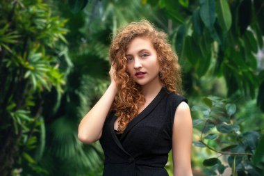 Siyah bluzlu, kıvırcık saçlı güzel bir kızın portresi. Yazın yeşil bir bahçede.