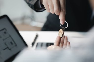 A home rental company employee is handing the house keys to a customer who has agreed to sign a rental contract, explaining the details and terms of the rental. Home and real estate rental ideas.