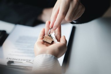 Bir ev kiralama şirketi çalışanı kira sözleşmesi imzalamayı kabul eden bir müşteriye kira sözleşmesinin detaylarını ve şartlarını açıklayan ev anahtarlarını teslim ediyor. Ev ve gayrimenkul kiralama fikirleri.