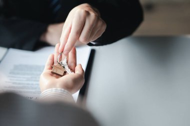 A home rental company employee is handing the house keys to a customer who has agreed to sign a rental contract, explaining the details and terms of the rental. Home and real estate rental ideas.