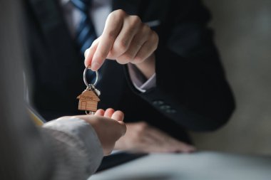 Bir ev kiralama şirketi çalışanı kira sözleşmesi imzalamayı kabul eden bir müşteriye kira sözleşmesinin detaylarını ve şartlarını açıklayan ev anahtarlarını teslim ediyor. Ev ve gayrimenkul kiralama fikirleri.