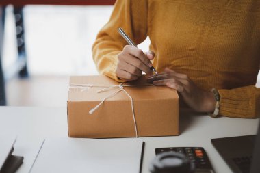 Bir e-ticaret şirketini işleten kadın, onlara göndermeden önce müşterilerin bir listesini kağıda yazıyor. Web sitelerinde ve sosyal medyada bir e-ticaret şirketi işletiyor. Çevrimiçi ürün satma kavramı.
