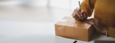 Bir e-ticaret şirketini işleten kadın, onlara göndermeden önce müşterilerin bir listesini kağıda yazıyor. Web sitelerinde ve sosyal medyada bir e-ticaret şirketi işletiyor. Çevrimiçi ürün satma kavramı.