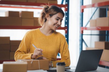 Bir e-ticaret şirketini işleten kadın, onlara göndermeden önce müşterilerin bir listesini kağıda yazıyor. Web sitelerinde ve sosyal medyada bir e-ticaret şirketi işletiyor. Çevrimiçi ürün satma kavramı.