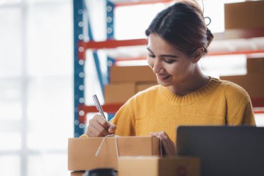 Bir e-ticaret şirketini işleten kadın, onlara göndermeden önce müşterilerin bir listesini kağıda yazıyor. Web sitelerinde ve sosyal medyada bir e-ticaret şirketi işletiyor. Çevrimiçi ürün satma kavramı.