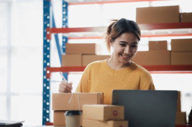 Bir e-ticaret şirketini işleten kadın, onlara göndermeden önce müşterilerin bir listesini kağıda yazıyor. Web sitelerinde ve sosyal medyada bir e-ticaret şirketi işletiyor. Çevrimiçi ürün satma kavramı.