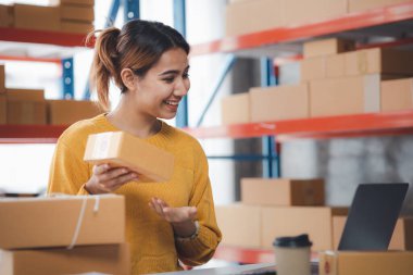 A beautiful Asian business owner opens an online store, she is checking orders from customers, sending goods through a courier company, concept of a woman opening an online business.