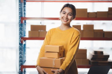 A beautiful Asian business owner opens an online store, she is checking orders from customers, sending goods through a courier company, concept of a woman opening an online business.