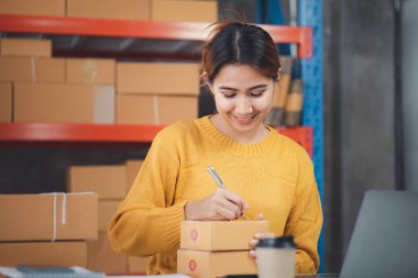 Online store salesperson is writing a customer's shipping address on parcel box before sending it to private carrier for delivery to customer. The idea of opening an online store and packing products.