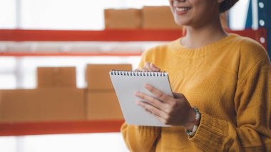 Bir çevrimiçi mağazanın sahibi, paketlenmiş ürünlerin siparişlerini web sitesinden sipariş edildiği gibi müşterilere teslimata hazırlamak için kontrol etmektedir. Çevrimiçi satış ve online alışveriş kavramları.