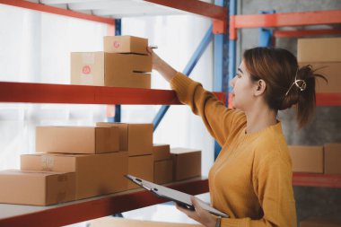 Bir çevrimiçi mağazanın sahibi, paketlenmiş ürünlerin siparişlerini web sitesinden sipariş edildiği gibi müşterilere teslimata hazırlamak için kontrol etmektedir. Çevrimiçi satış ve online alışveriş kavramları.