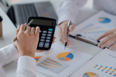 Bir şirketin mali belgelerindeki rakamları hesaplamak için hesap makinesi kullanan bir işadamı, şirketin nasıl büyüyeceğini planlamak için tarihsel finansal verileri analiz ediyor. Mali konsept.