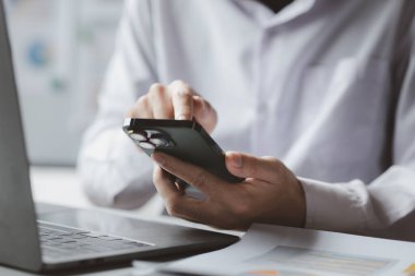 Business man looking at financial information from a mobile phone, he is checking company financial documents, he is an executive of a startup company. Concept of financial management.
